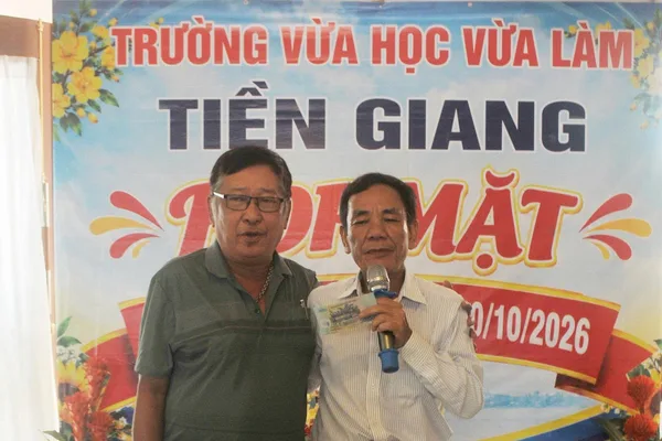 Hai người chụp ảnh lưu niệm trước phông họp mặt trường 10/10/2026